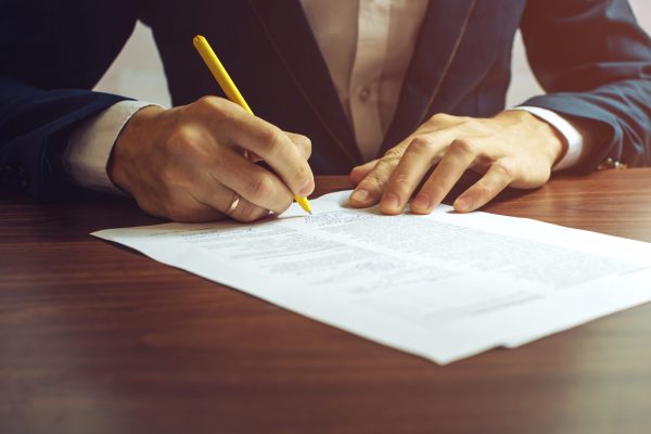 Man businessman signs documents with a pen making the signature sitting at the desk in the light. With retro effect.